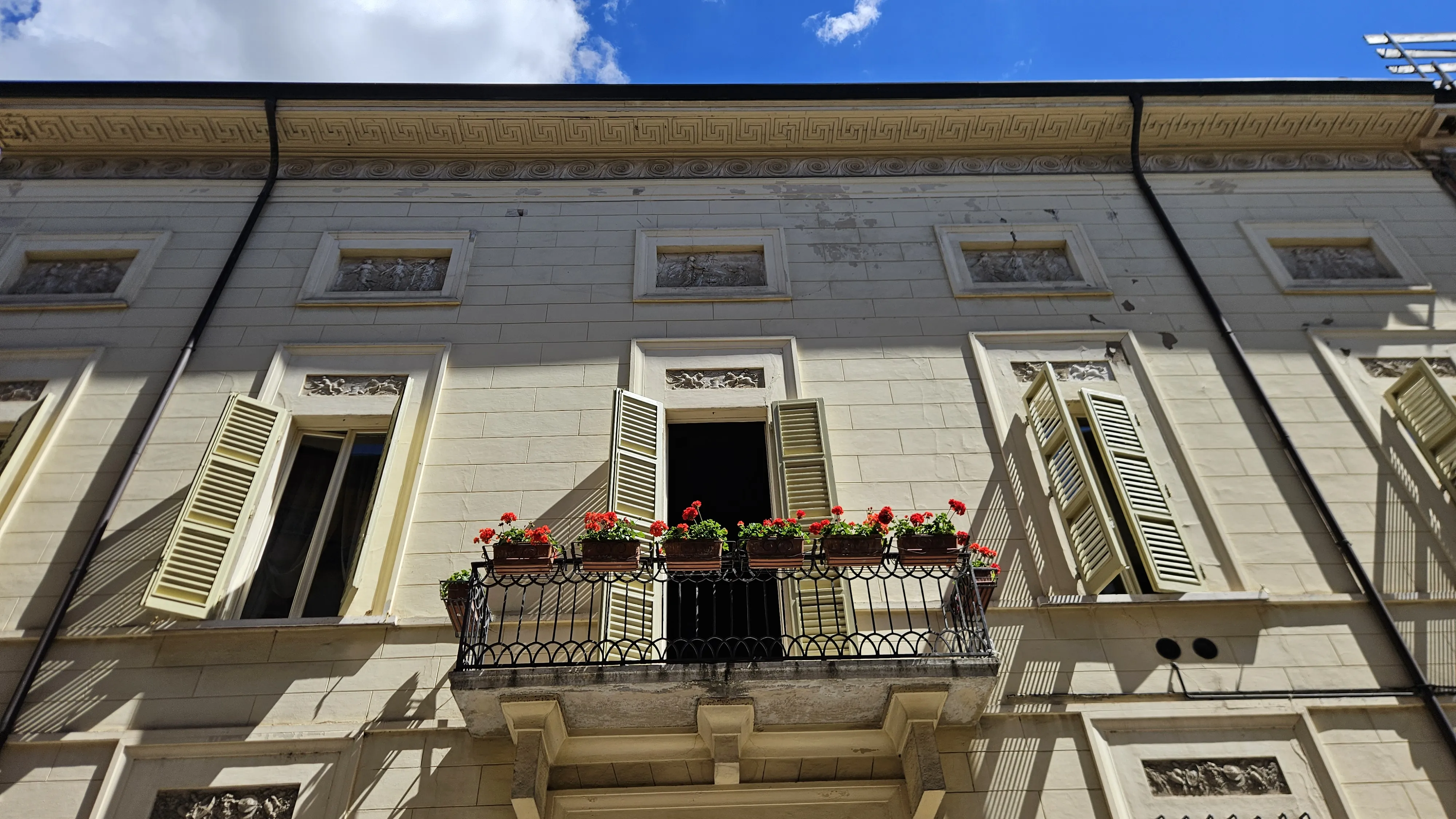 Balcone fiorito con gerani rossi, architettura storica di Faenza, Emilia-Romagna